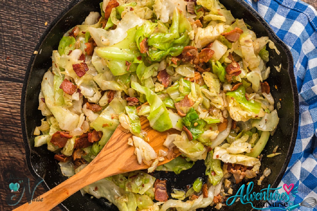 Southern fried cabbage with crispy bacon and onions in a skillet with a wooden spoon.