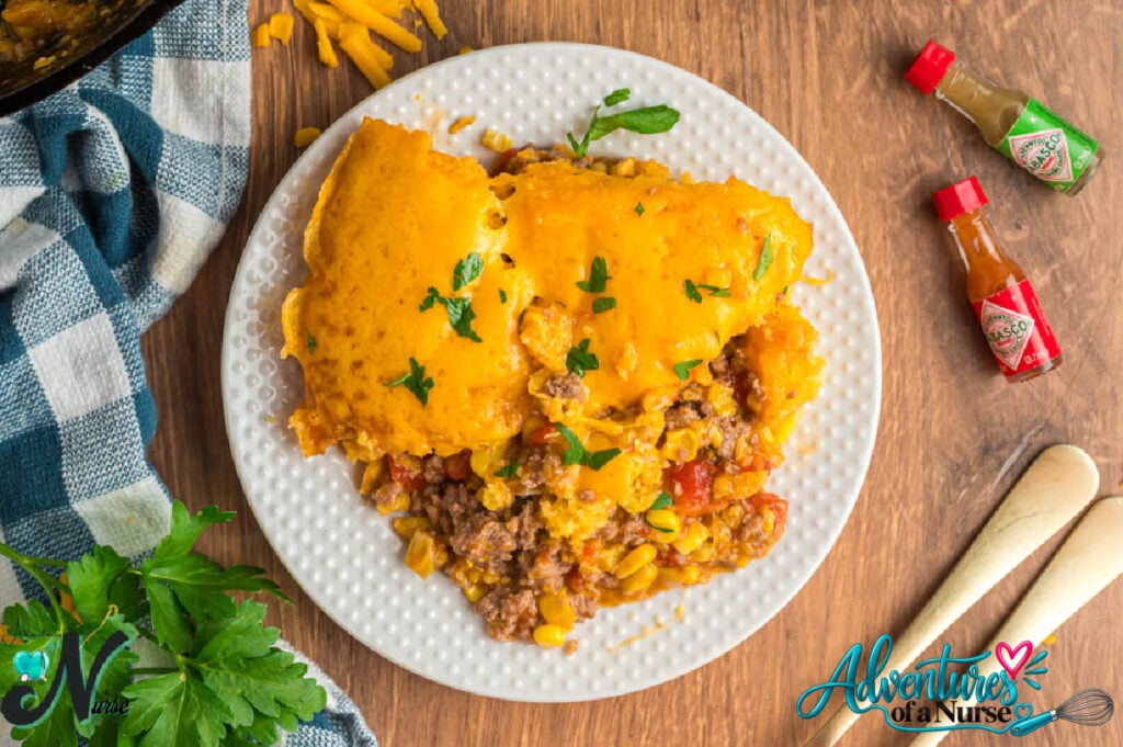 Mexican cornbread casserole with golden cheesy cornbread topping and seasoned ground beef filling served on a white plate.