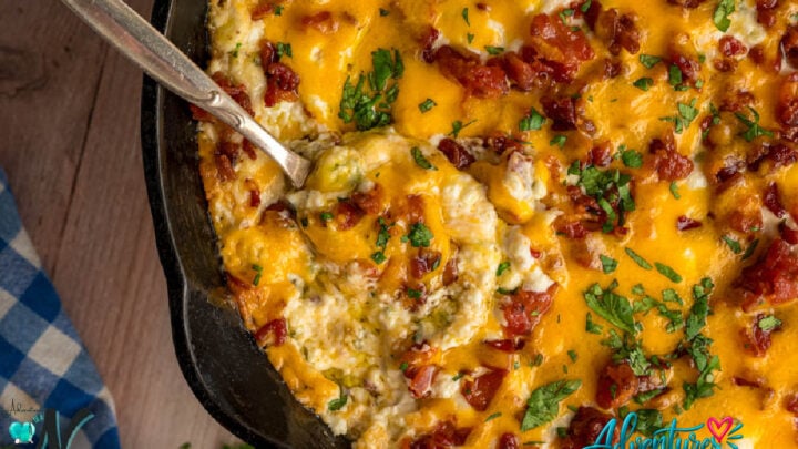 Hot jalape&ntilde;o popper dip topped with melted cheddar cheese, crispy bacon, and jalape&ntilde;os in a baking dish with a spoon.