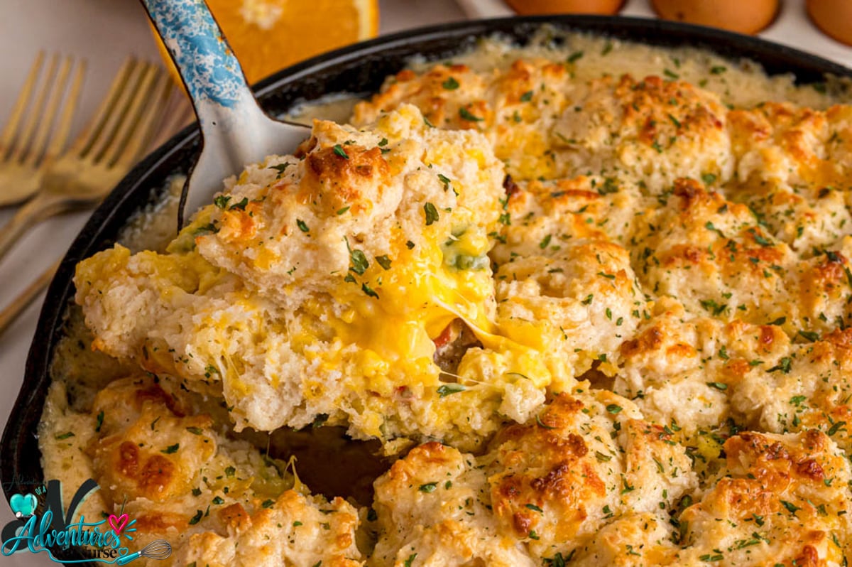 Breakfast pot pie with golden biscuit topping and cheesy scrambled eggs being lifted from a cast iron skillet.