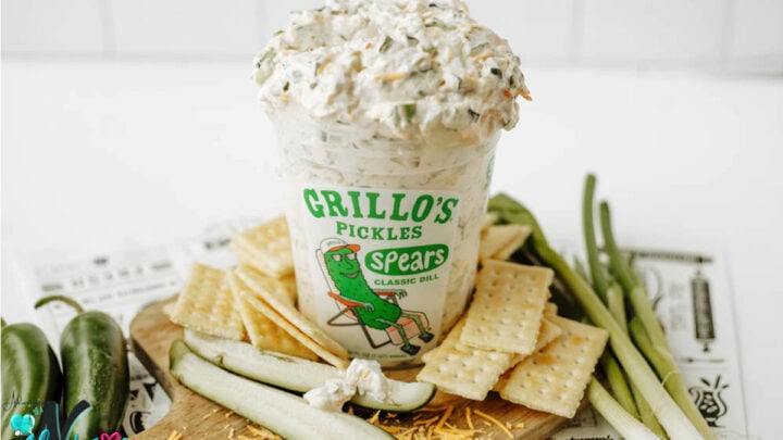 Homemade Grillo's pickle dip in a bowl topped with chopped pickles and herbs, served with crackers and whole pickles.