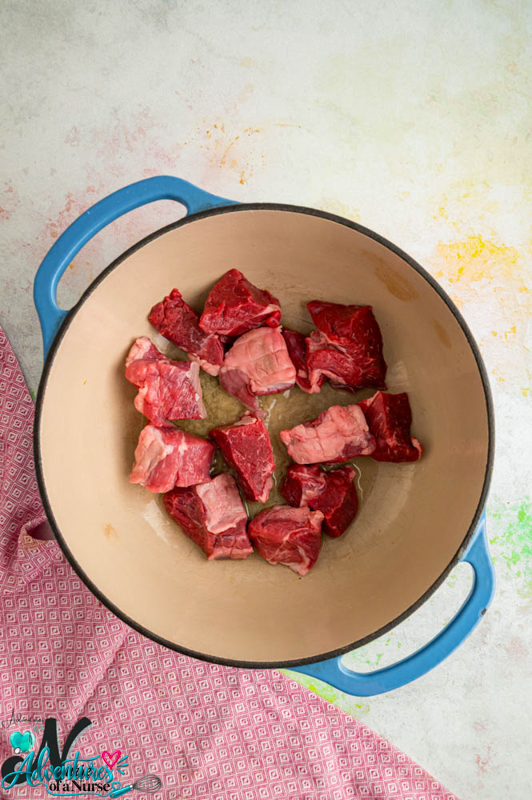 Raw chunks of lamb in a Dutch oven with olive oil for homemade lamb dog food.