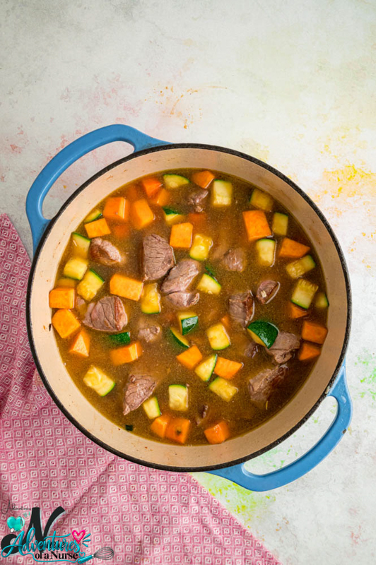 Lamb, brown rice, and diced vegetables mixed together in a Dutch oven before simmering.